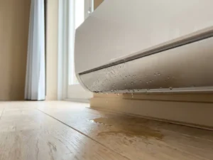Witte wandgemonteerde airconditioning lekt waterdruppels op houten vloer in modern Nederlands interieur