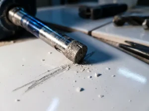 Diamond drill slides sideways over white ceramic tile and causes scratch damage with ceramic dust and splinters.