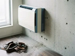 Wandgemonteerde airconditioning boven betonnen muur met boorstelsel op de vloer en een versleten leren gereedschapsriem ernaast.